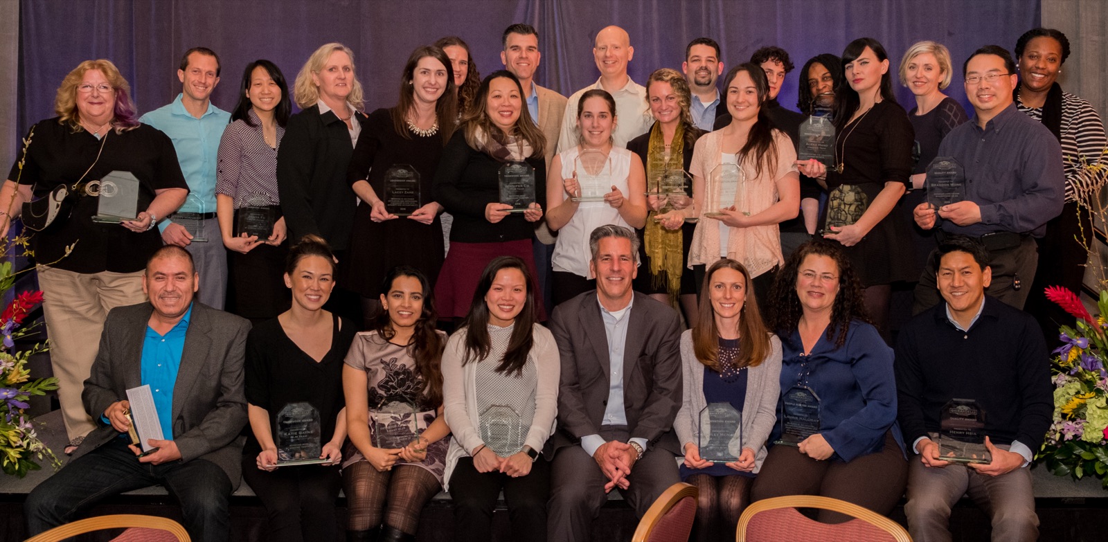 About two dozen Ghirardelli employees on stage at the company's 2016 awards dinner, each holding a glass award.